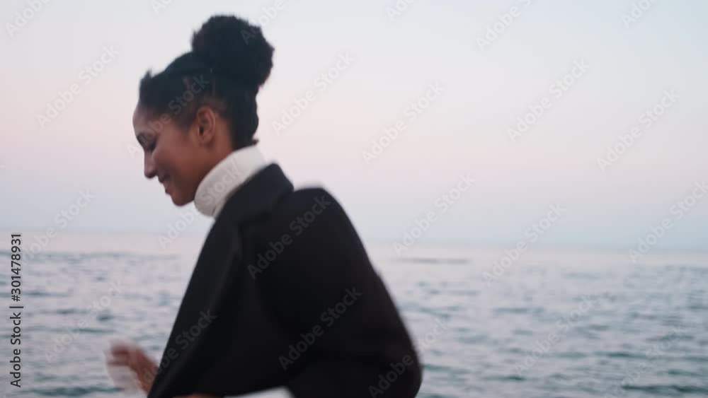 Medium shot of beautiful stylish African American girl joyfully running by the sea Medium shot of beautiful stylish African American girl joyfully running by the sea