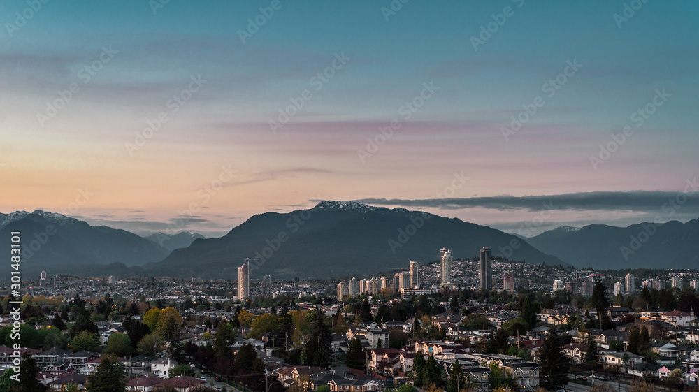 View of East Vancouver and downtown of Brentwood, Burnaby skylines with mount Seymour backdrop lit by last sun rays before sunset