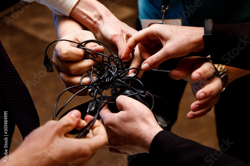 Many male hands try to untangle the wires.