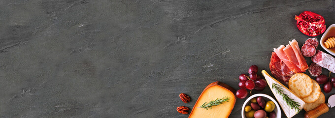 Selection of cheese and meat appetizers. Corner border banner, above view on a slate stone background with copy space.