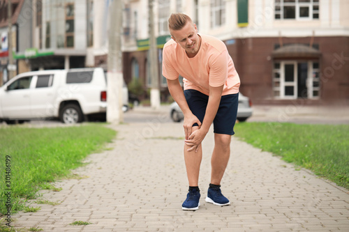 Young sporty man suffering from pain in knee outdoors