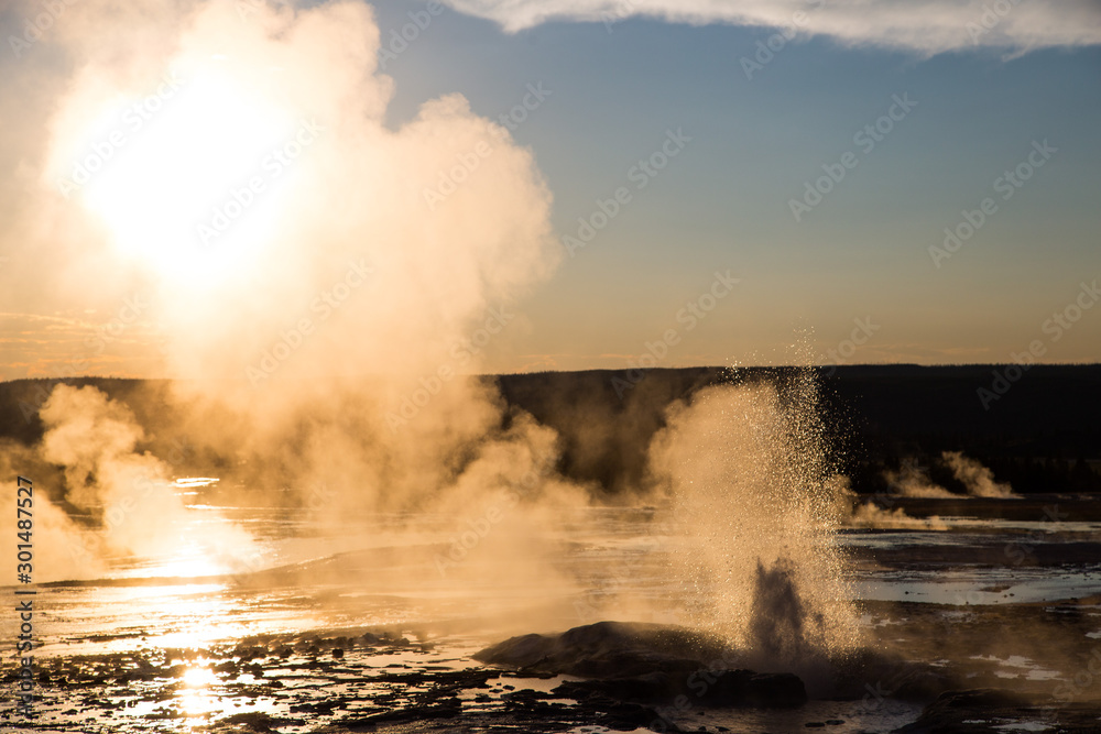 Spasm geyser during eruption with setting sun and steam