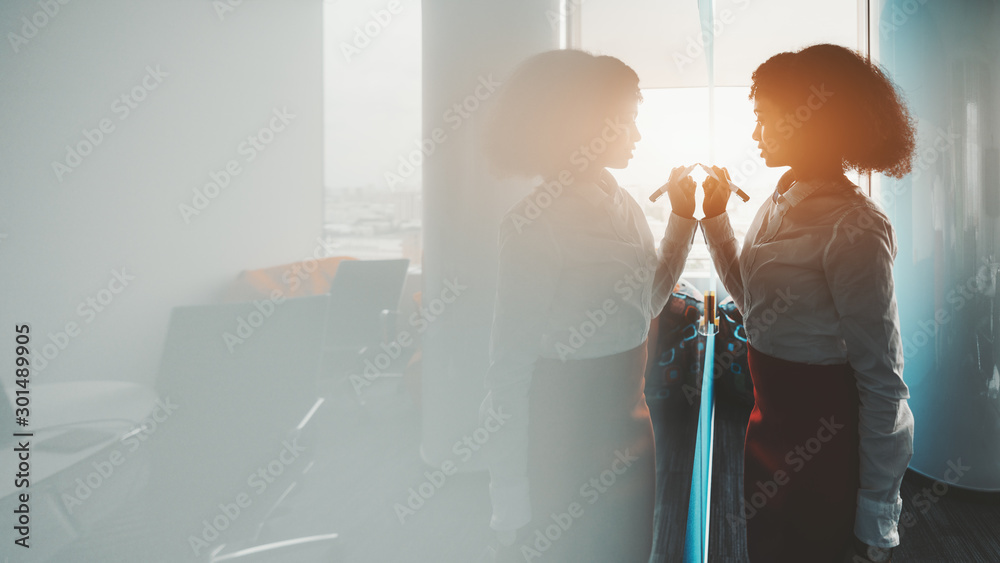 Side wide-angle view of a dazzling African-American woman entrepreneur with a curly afro hair in the meeting room writing on the board using a marker; a big copy space area on the left for your text - obrazy, fototapety, plakaty 