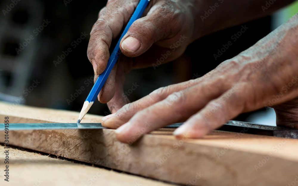 Close-up of a carpenter's hand, using a ruler and a pencil to make wood.