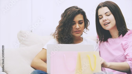 Friends sitting on the sofa side by side, with laptop, choosing what to buy onlone, but showing that they are short of money. Blurred bags on the forefront. photo