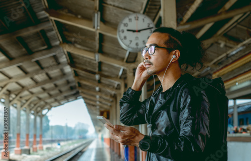 An Asian man with his mobile is waiting for a late train.