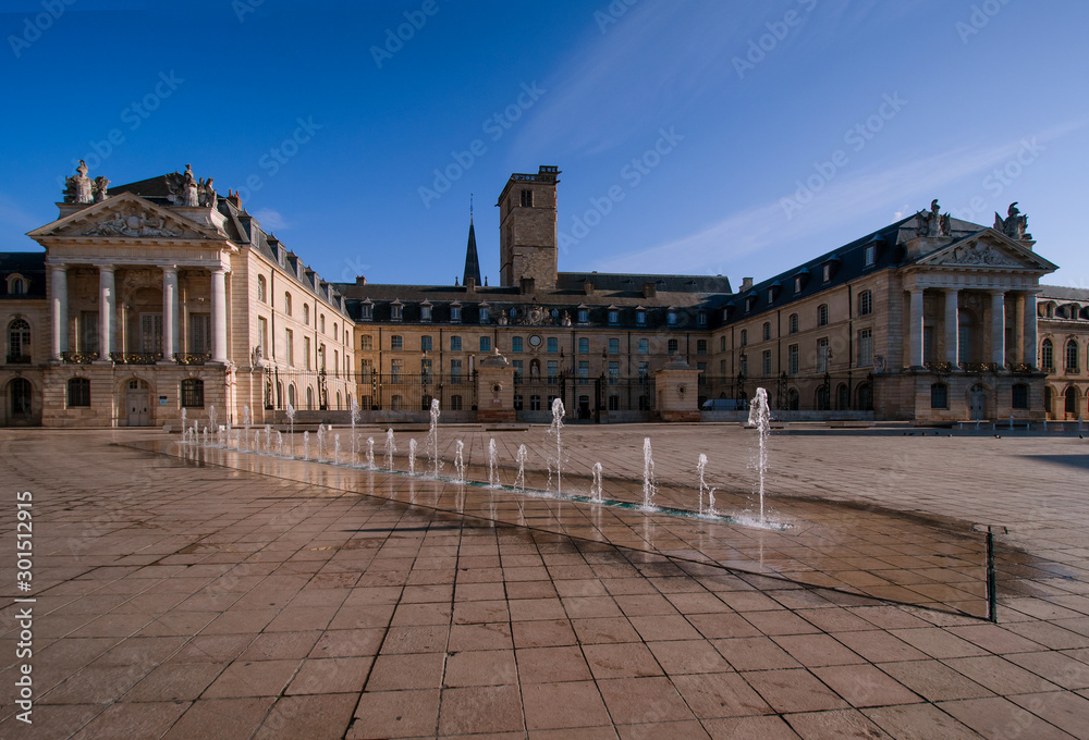Palace of the Dukes of Burgundy in the morning. Sky is blue. City of Dijon. France. In the foreground there is an area covered with stone tiles and a fountain.