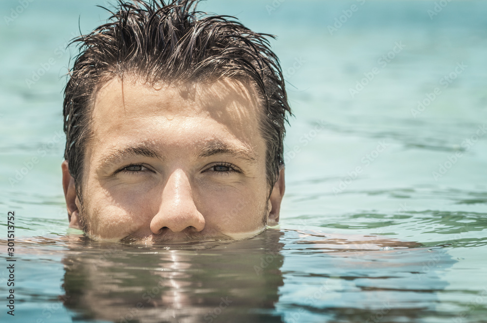 Attractive young man  swimming in the azure sea with half face submerged underwater