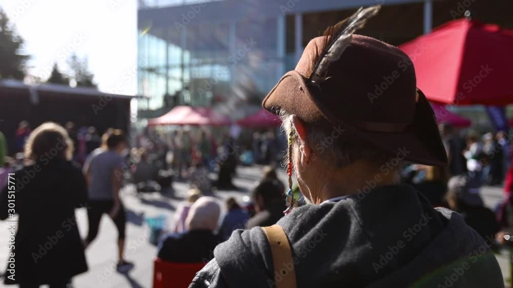 An elderly male activist in old fashioned mountaineers hat with selective focus is seen from the back listening to speeches at environmental rally An elderly male activist in old fashioned mountaineers hat with selective focus is seen from the back listening to speeches at environmental rally
