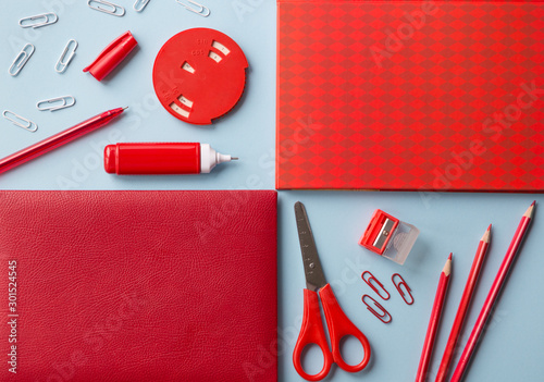 Flat lay red office supplies on a blue background. Notebook, pen, pencil, paper clips, planer and corrector