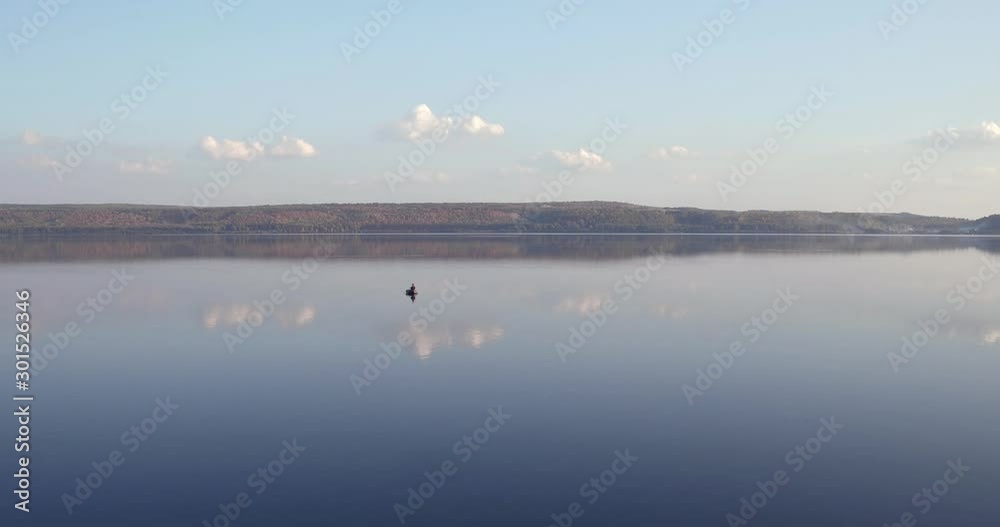 Fishermen alone in a boat swimming on a big lake / mountains background - aerial drone view Fishermen alone in a boat swimming on a big lake / mountains background - aerial drone view