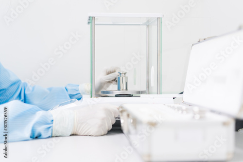 The operator's hand is holding stainless steel calibration weight to place on the analytical balance pan for the calibration test, concept of quality control laboratory in pharmaceutical industry.