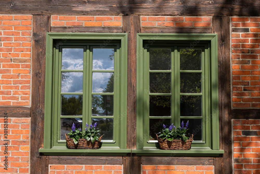 Windows with green frames and decorated by flowers in baskets, .surrounded by bricks wall. Windows with green frames and decorated by flowers in baskets, .surrounded by bricks wall.