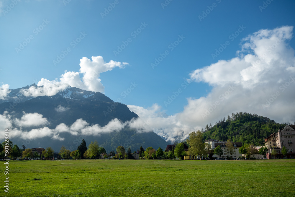 Obraz premium Beautiful view of green field at interlaken town on mountains and clouds blue sky background with copy space