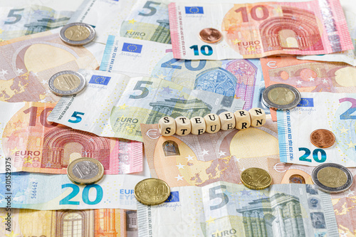 Steuern Schriftzug über Euro Geldscheinen und Münzen, Nahaufnahme
