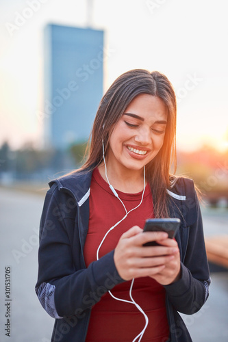 Modern young woman with cellphone making pause during jogging / exercise.