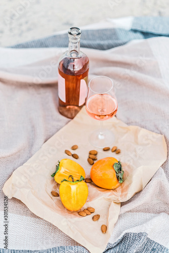 Picnic on the beach with persimmons, almond and bottle of rose wine on beige blanket. photo