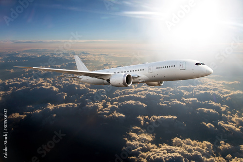 White passenger plane in flight. The plane flies high above the clouds through the sun rays.
