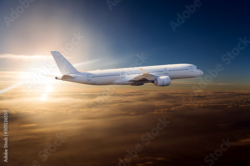The passenger plane flies over the clouds during sunset. Side view of passenger long range aircraft.