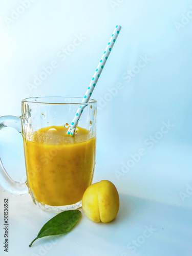 a glass of fresh yellow smoothie with a straw. Summer and tropical smoothies. Cold blended drinks, fruit smoothie.