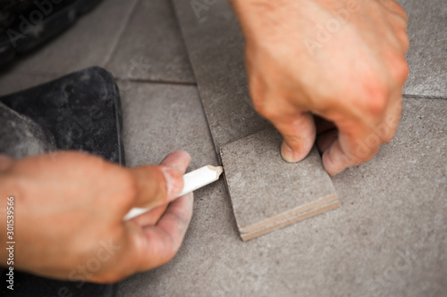 A construction worker marks the ceramic tile he wants to cut.