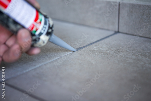 The hand of a construction worker filling the gap between ceramic tiles with silicone photo