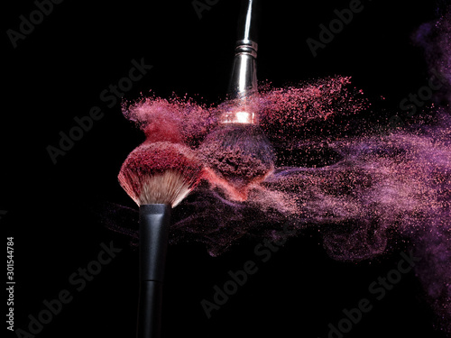 closeup cosmetic brush releasing a cloud of sparkling powder over a black background 