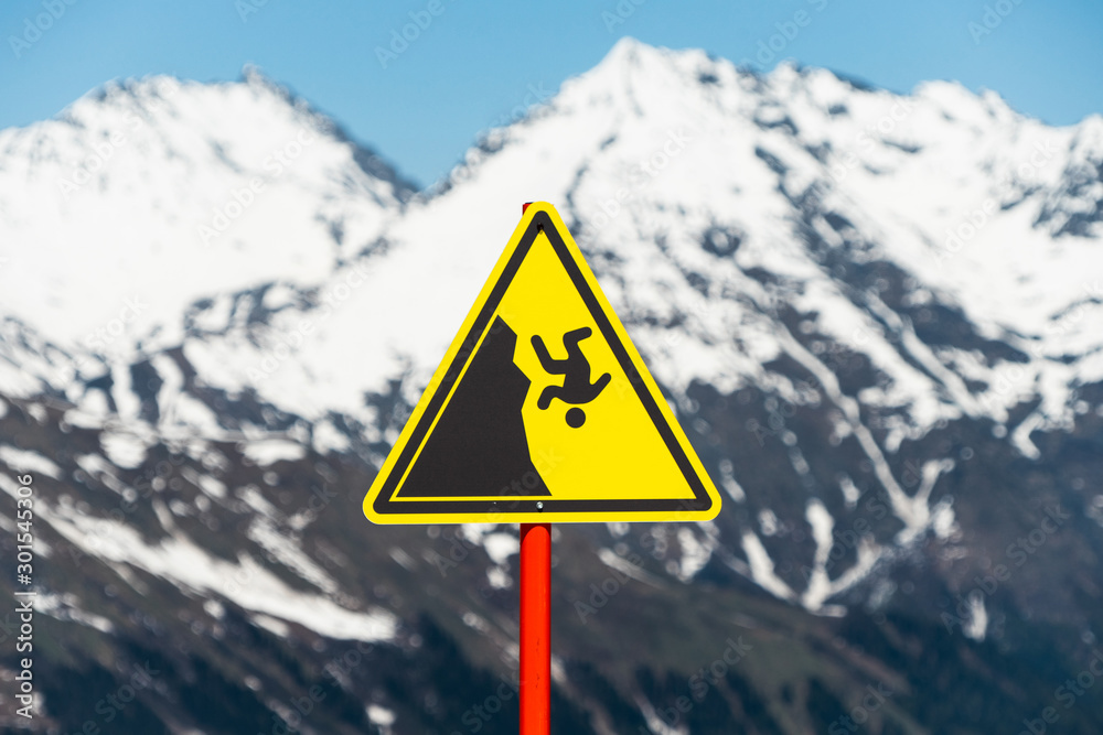 Yellow danger sign in the mountains. Hiking Safety Warning. Caution of falling from the Mountain. Yellow danger sign in the mountains. Hiking Safety Warning. Caution of falling from the Mountain.
