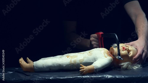 male hands saw off a scary dolls head, halloween
