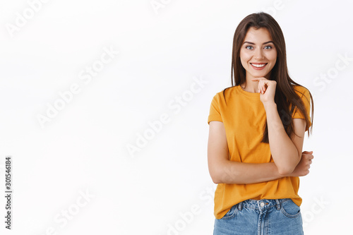 Curious and intrigued young woman listen interesting story, touch chin and smiling impressed, standing thoughtful consider to buy awesome new product as watching advertisement, white background