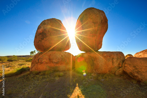 Australia, Northern Territory. Aboriginal land in Red Centre. Sunbeams sky at sunrise behind iconic the Eggs of mythical Rainbow Serpent at Karlu Karlu - Devils Marbles Conservation Reserve. photo