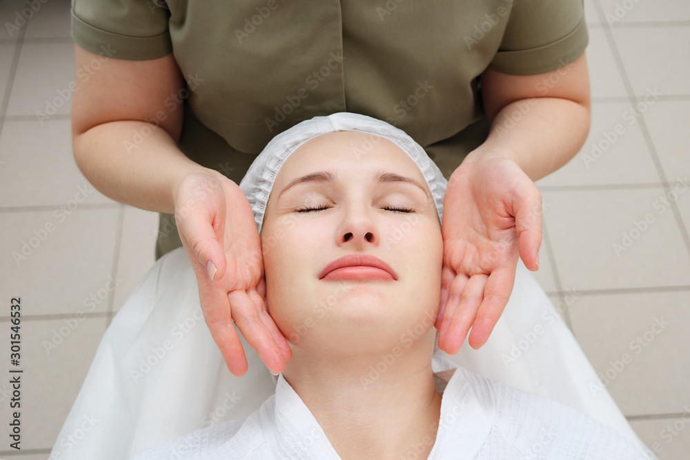masseuse hands move slowly doing calming face massage to beautiful girl client in medical center view from above masseuse hands move slowly doing calming face massage to beautiful girl client in medical center view from above