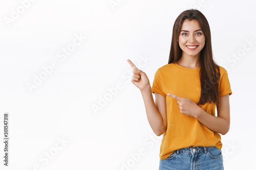 Pleasant, friendly-looking pretty caucasian woman in yellow t-shirt pointing upper left corner, help customer find way, recommend product or event promo, standing white background confident photo