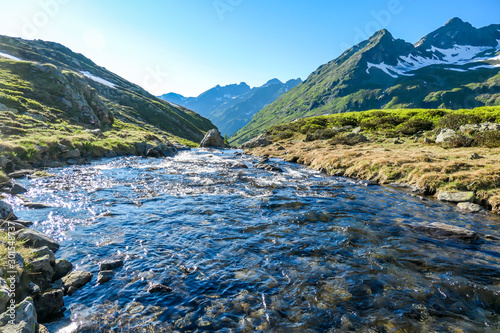 A serene view on snowy mountain from a small stream s side. The stream starts it s long way to the sea. Tall glacier towering above the landscape. Spring in the alpine valley.