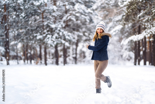 Happy young woman plays with a snow in sunny winter day. Girl enjoys winter, frosty day. Playing with snow on winter holidays, a woman throws white, loose snow into the air. Walk in winter forest.