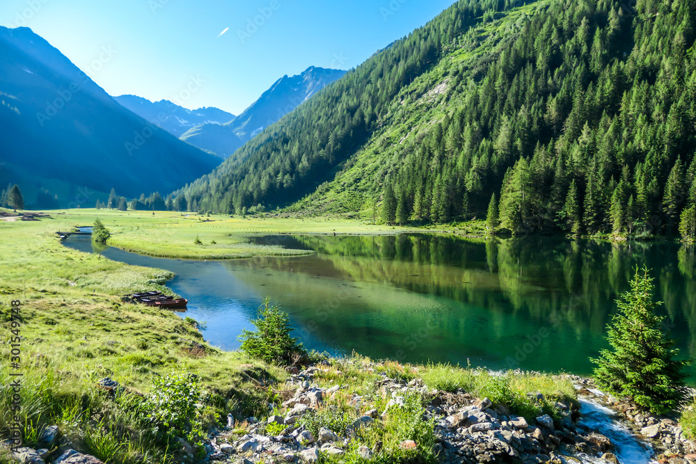 A calm alpine lake. The lake is surrounded with tall mountains. The surface of the lake is calm, it reflects the mountains and sky. Clear and sunny day. Schladming region, Austria