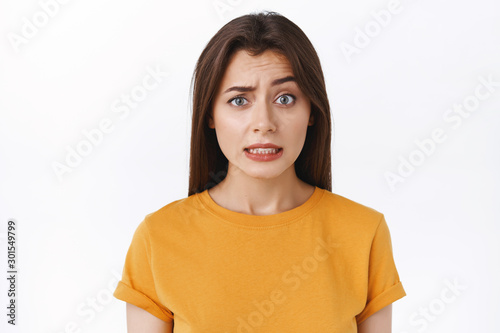 Awkward and worried cute embarrassed woman apologizing, cringe and frowning bothered as admit her mistake, standing nervous over white background, remember something humiliating