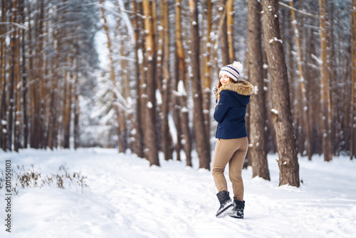 Portrait of young beautiful girl with long hair, in a blue jacket and knitted hat and mittens posing in sunny winter day. Fashion young woman in the winter forest. Christmas, winter holidays concept.  © maxbelchenko