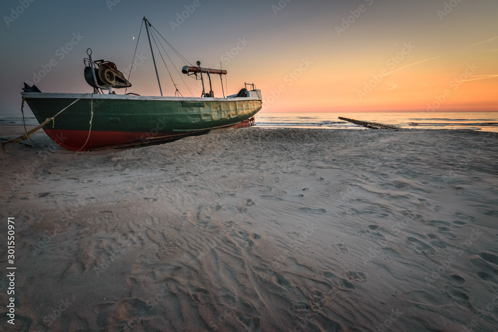 Old green and ref fishermen's boat stranded on the sandy beach at sunset Latvia Old green and ref fishermen's boat stranded on the sandy beach at sunset Latvia
