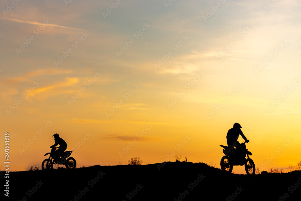 Two Black silhouette Motocross rider on a motorcycle in front of colorful sunset