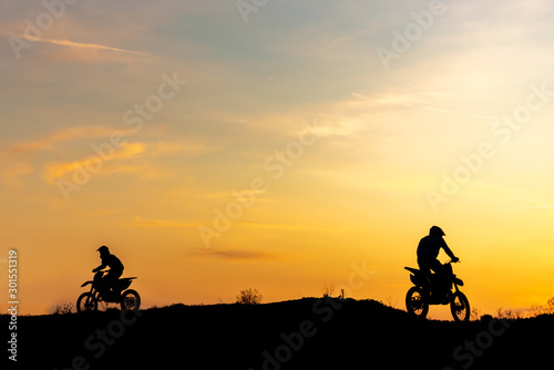 Two Black silhouette Motocross rider on a motorcycle in front of colorful sunset