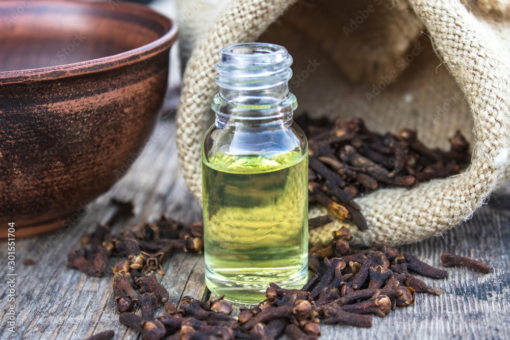 Spice clove essential oil in a glass bottle on old wooden boards near dry clove spices. Spice clove essential oil in a glass bottle on old wooden boards near dry clove spices.
