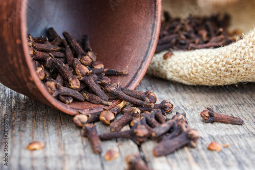 A pile of dried cloves lies on old wooden boards next to a bowl of spices.