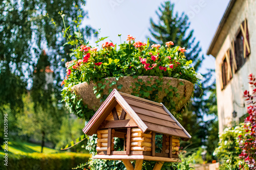 Bird house made of wood next to a pot full of flowers and plants.