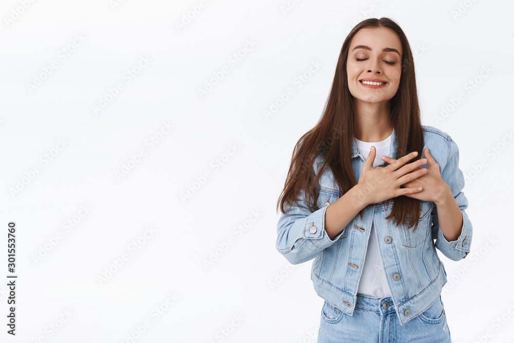 Uplifted, dreamy caucasian woman in denim jacket, jeans, touch her heart, close eyes and smiling with lovely expression, admire someone or feeling romantic feelings, standing white background Uplifted, dreamy caucasian woman in denim jacket, jeans, touch her heart, close eyes and smiling with lovely expression, admire someone or feeling romantic feelings, standing white background