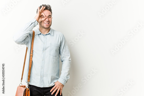 Young handsome business man excited keeping ok gesture on eye.