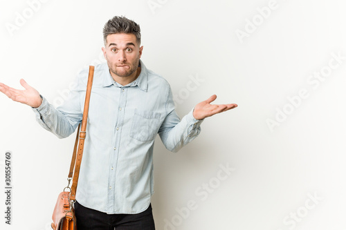 Young handsome business man confused and doubtful shrugging shoulders to hold a copy space.