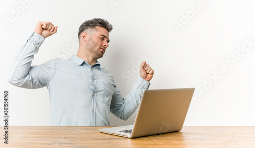 Young handsome man working with his laptop stretching arms, relaxed position.