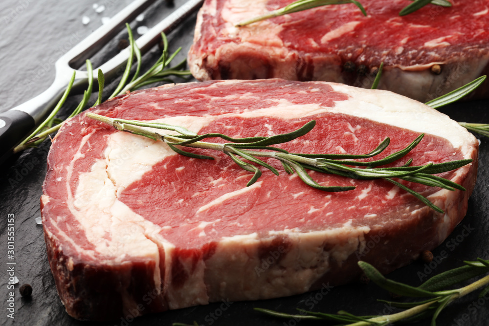 Raw fresh meat Ribeye Steak, seasoning and meat fork on rustic background