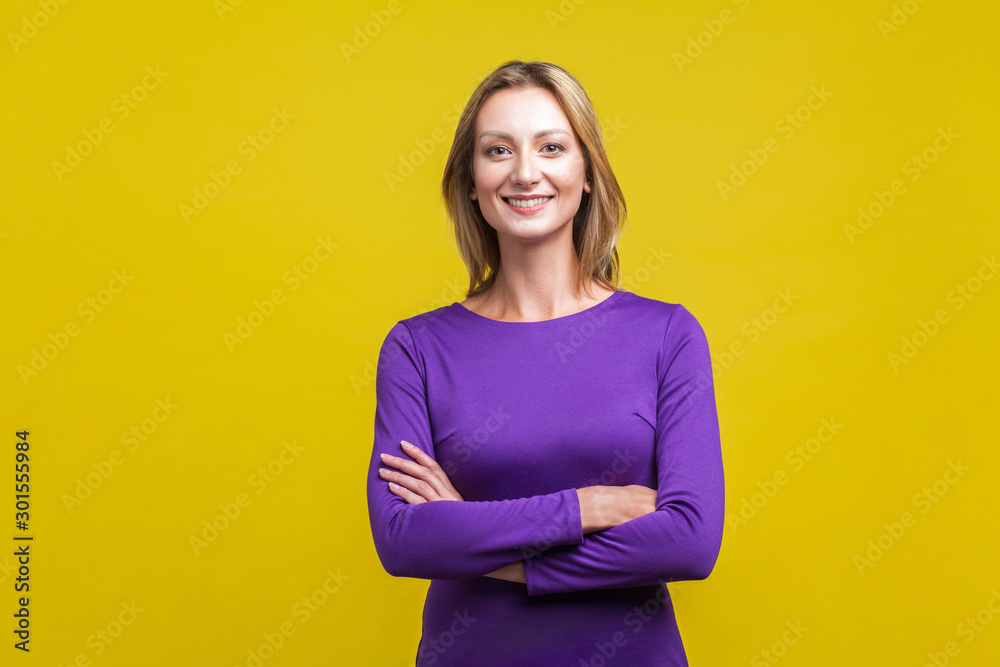 © khosrork - Portrait of happy successful businesswoman in tight purple dress standing with crossed hands, looking at camera with charming and joyous toothy smile. indoor studio shot isolated on yellow background © khosrork - Portrait of happy successful businesswoman in tight purple dress standing with crossed hands, looking at camera with charming and joyous toothy smile. indoor studio shot isolated on yellow background